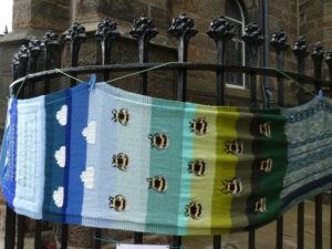 Knitted bees on a blue and green background, tied to railings