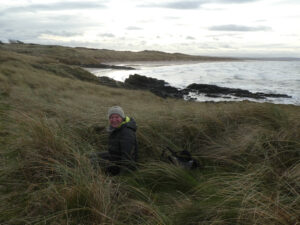 A woman sitting in long grass beside the sea