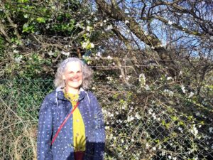 A woman smiling beside a hedge in blossom