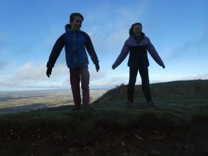 2 children silhouetted against the blue sky being blown in the wind