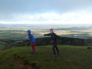 Two walkers with arms outstretched leaning into the wind